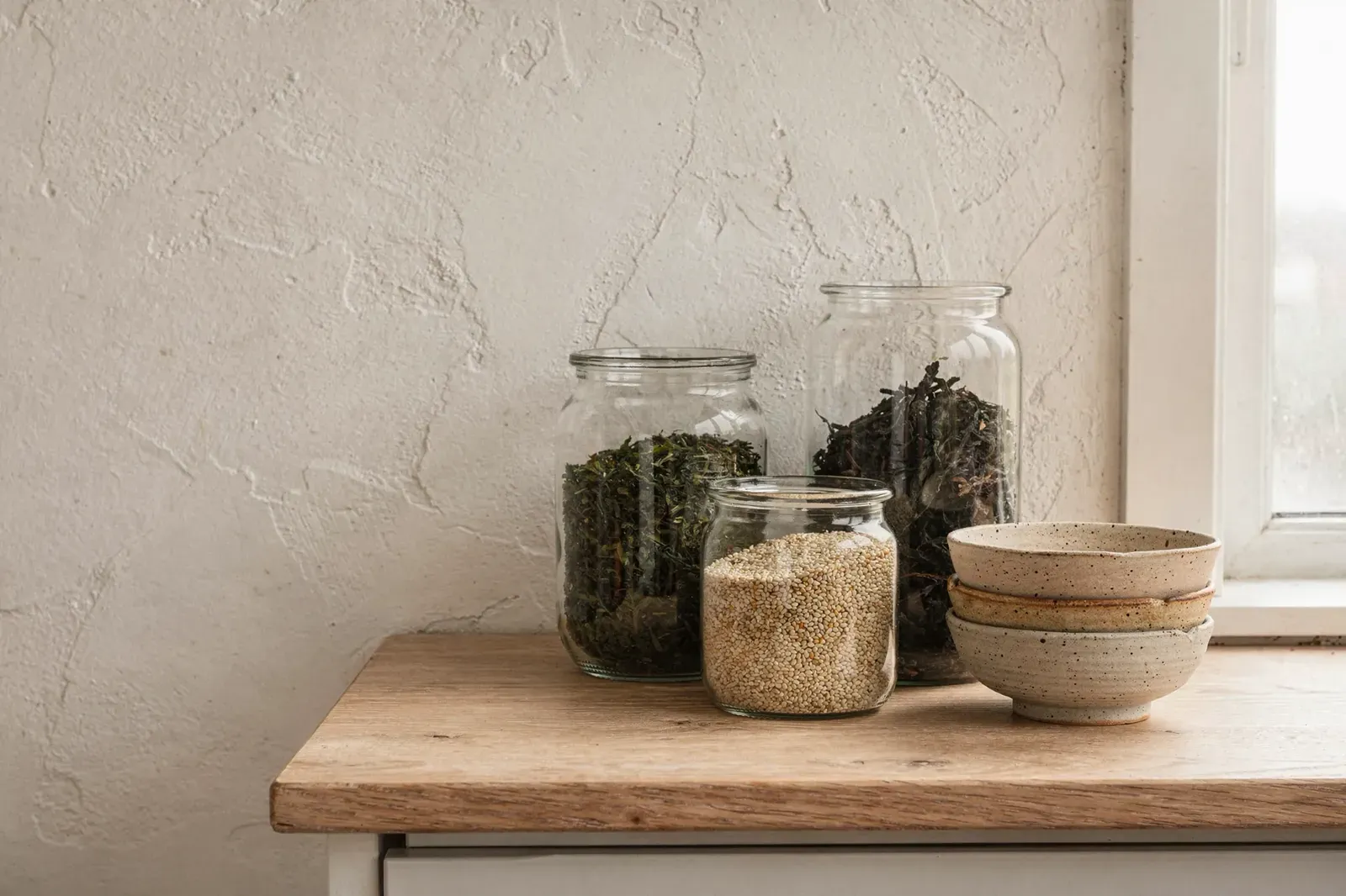 Glass jars of tea and seaweed beside ceramic bowls on a wooden counter in a Swedish kitchen