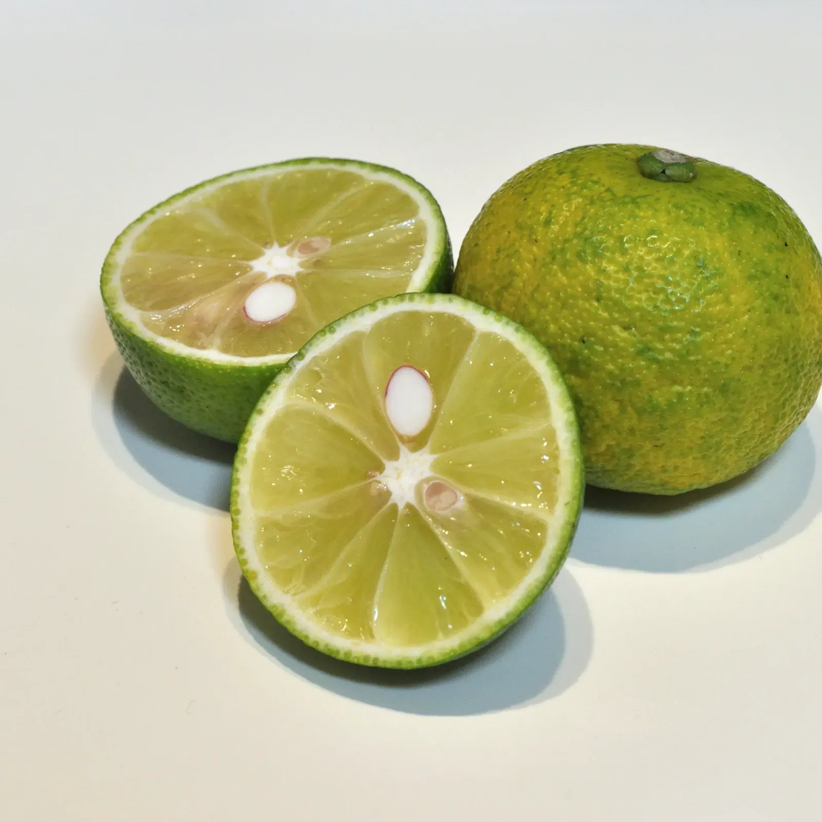 Sudachi, one whole fruit and two halves with pale green flesh