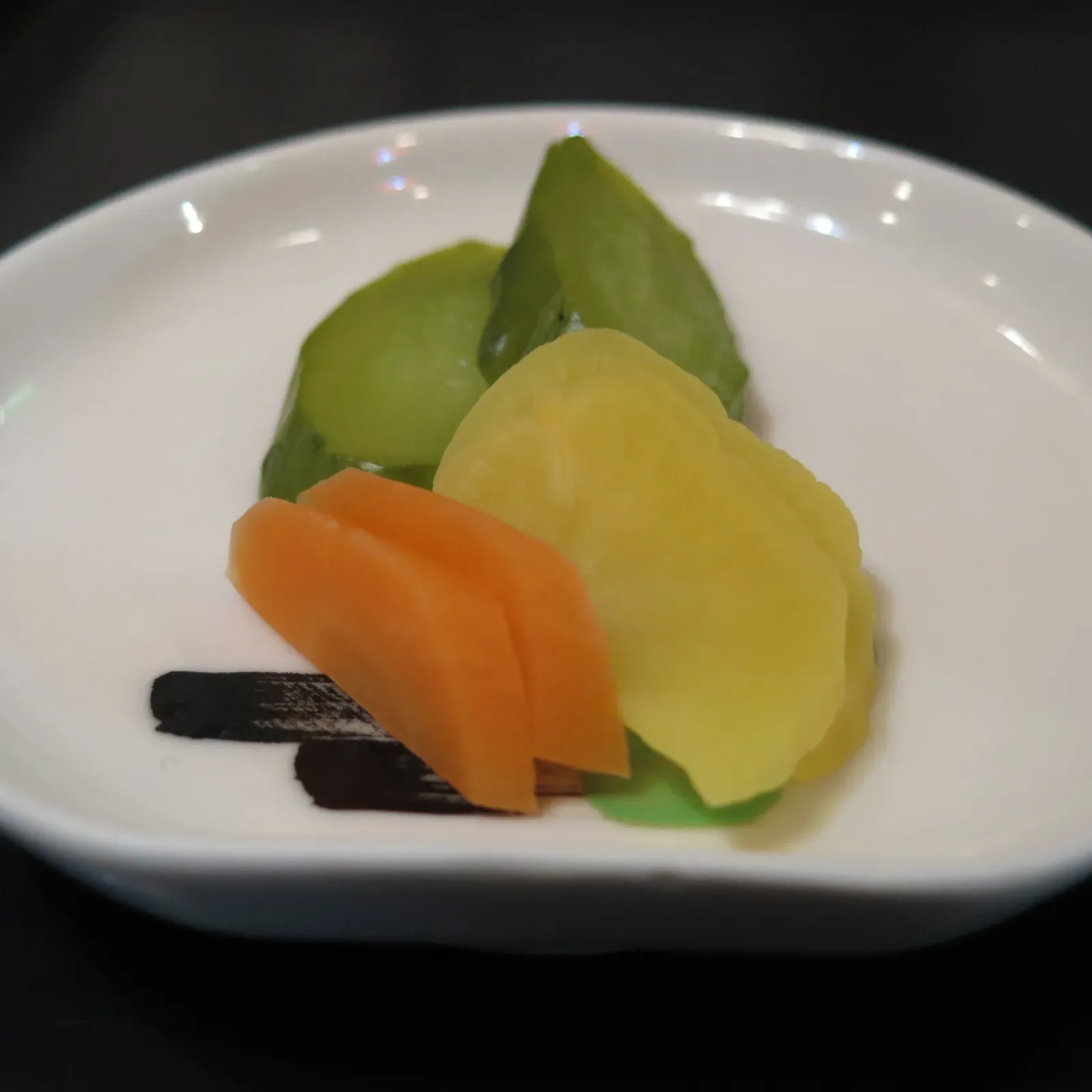 Small white dish of assorted tsukemono, cucumber, takuan, carrot, and kombu